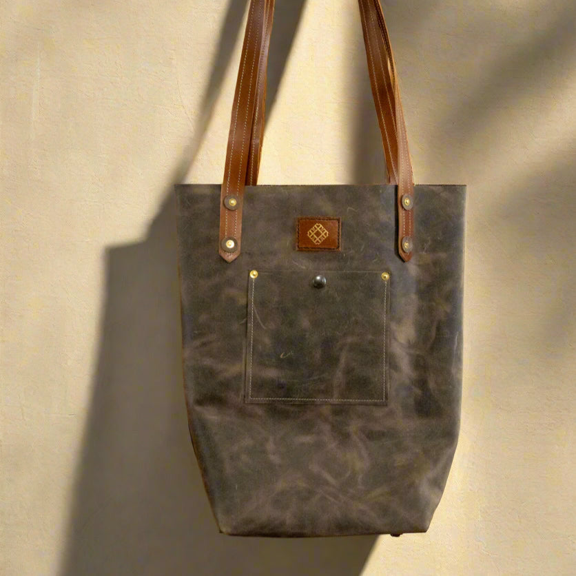 Brown leather tote bag with a visible brand logo hanging on a wall.